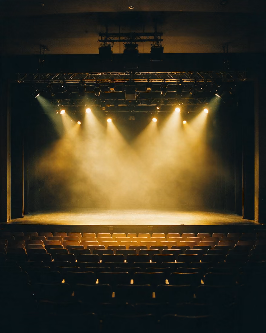 An empty auditorium an hour before doors: yellow stage light in the haze, seats still dark.