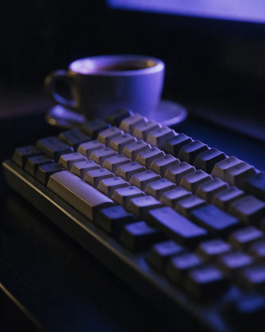 A mechanical keyboard shot low along the keys, washed in blue light from an off-frame screen.